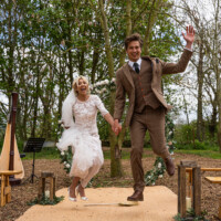 Jumping the broom is a really fun way to leap forward into your married life together with confidence and commitment Bride and groom jumping the broom at a woodland wedding venue in Northamptonshire